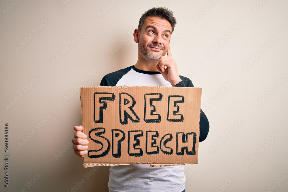 Young handsome man asking for rights holding banner with free speech message serious face thinking about question, very confused idea Young handsome man asking for rights holding banner with free speech message serious face thinking about question, very confused idea