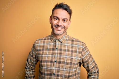 Young handsome man wearing casual shirt standing over isolated yellow background with a happy and cool smile on face. Lucky person.