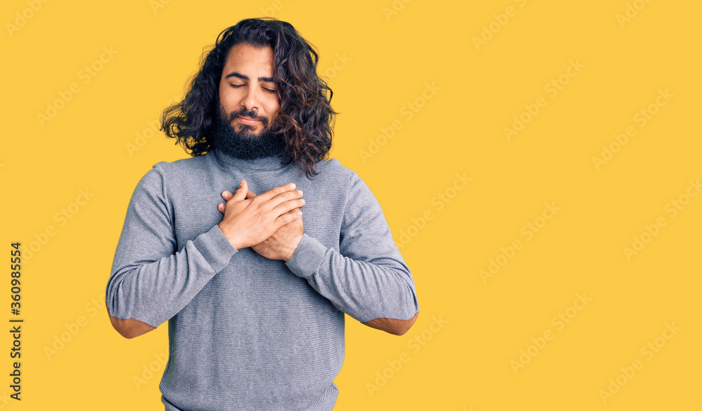 Young arab man wearing casual clothes smiling with hands on chest with closed eyes and grateful gesture on face. health concept. Young arab man wearing casual clothes smiling with hands on chest with closed eyes and grateful gesture on face. health concept.