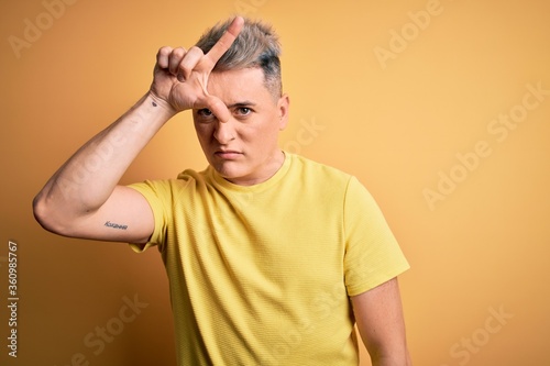 Young handsome modern man wearing yellow shirt over yellow isolated background making fun of people with fingers on forehead doing loser gesture mocking and insulting.
