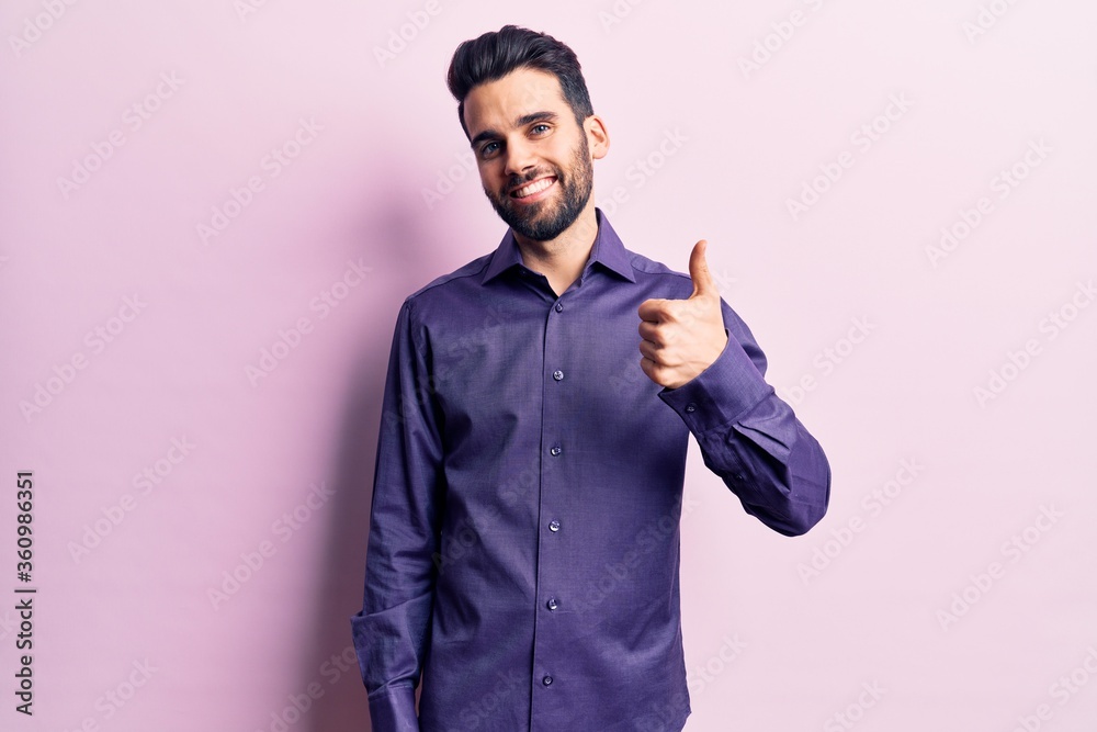 Young handsome man with beard wearing casual shirt doing happy thumbs up gesture with hand. approving expression looking at the camera showing success. Young handsome man with beard wearing casual shirt doing happy thumbs up gesture with hand. approving expression looking at the camera showing success.