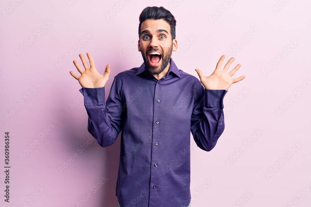 Young handsome man with beard wearing casual shirt celebrating crazy and amazed for success with arms raised and open eyes screaming excited. winner concept Young handsome man with beard wearing casual shirt celebrating crazy and amazed for success with arms raised and open eyes screaming excited. winner concept
