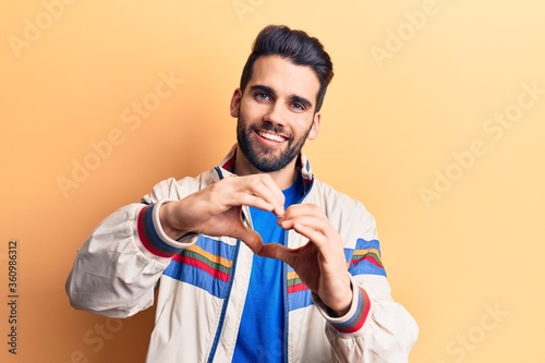 Young handsome man with beard wearing casual jacket smiling in love doing heart symbol shape with hands. romantic concept.