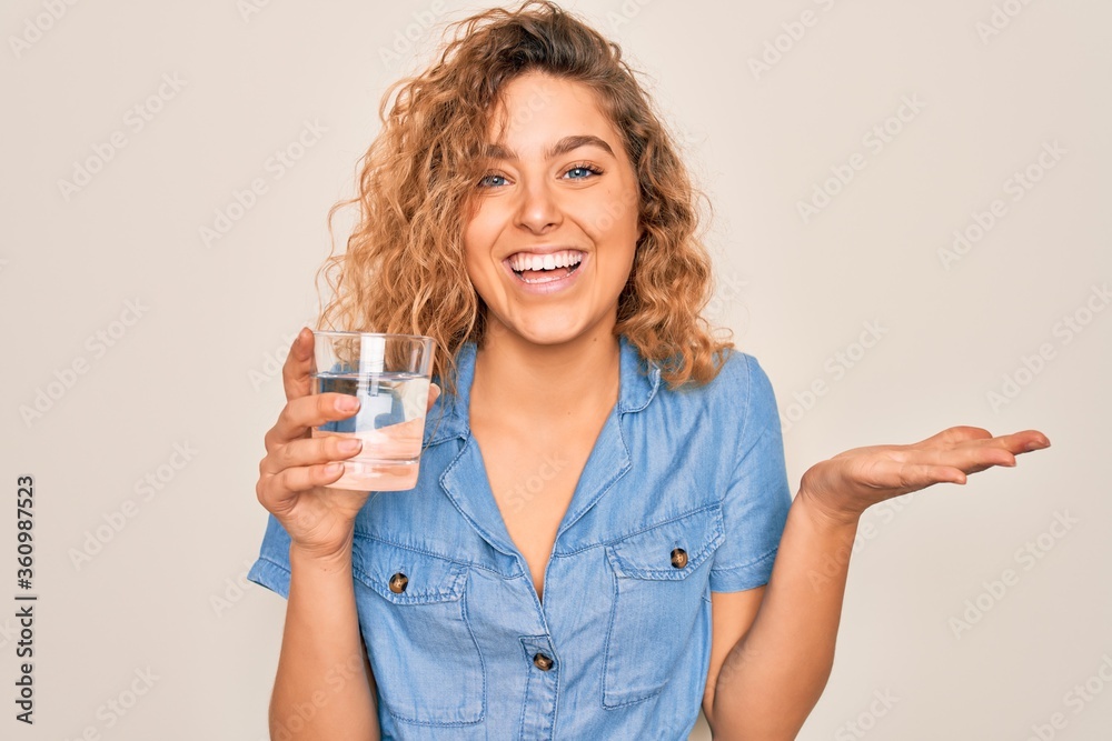 Young beautiful blonde woman with blue eyes drinking glass of water over white background very happy and excited, winner expression celebrating victory screaming with big smile and raised hands Young beautiful blonde woman with blue eyes drinking glass of water over white background very happy and excited, winner expression celebrating victory screaming with big smile and raised hands