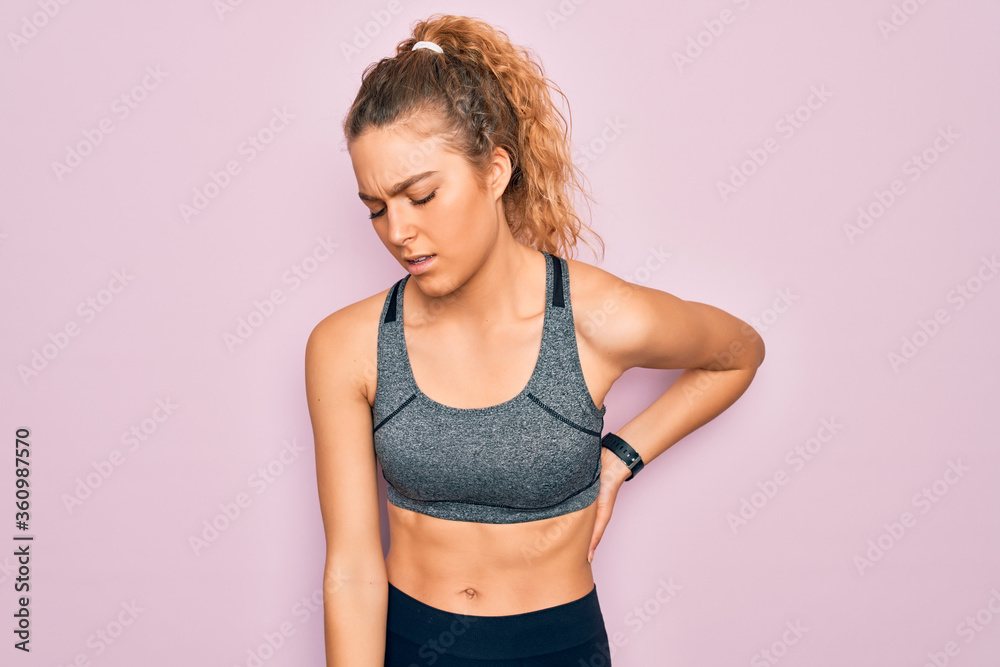 Young beautiful blonde sportswoman with blue eyes doing exercise wearing sportswear Suffering of backache, touching back with hand, muscular pain Young beautiful blonde sportswoman with blue eyes doing exercise wearing sportswear Suffering of backache, touching back with hand, muscular pain