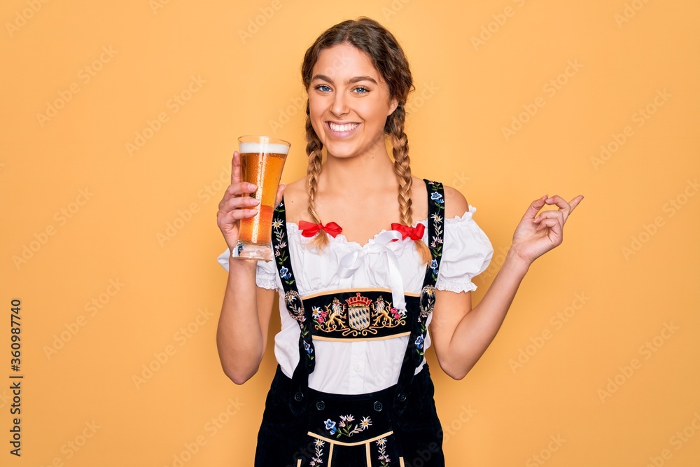 Beautiful blonde german woman with blue eyes wearing octoberfest dress drinking glass of beer very happy pointing with hand and finger to the side Beautiful blonde german woman with blue eyes wearing octoberfest dress drinking glass of beer very happy pointing with hand and finger to the side