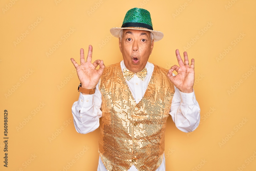Middle age senior grey-haired man wearing Brazilian carnival custome over yellow background looking surprised and shocked doing ok approval symbol with fingers. Crazy expression Middle age senior grey-haired man wearing Brazilian carnival custome over yellow background looking surprised and shocked doing ok approval symbol with fingers. Crazy expression