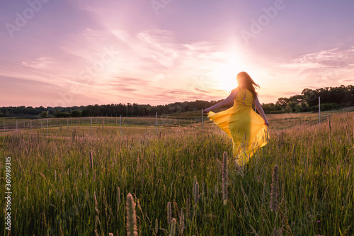 An Asian woman with long hair and yellow dress dances, rejoices, laughs under sunset with sunstar / sunburst