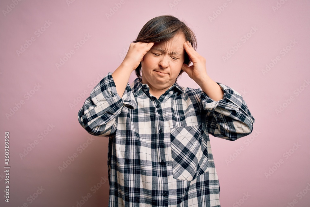 Young down syndrome woman wearing casual shirt over pink background suffering from headache desperate and stressed because pain and migraine. Hands on head. Young down syndrome woman wearing casual shirt over pink background suffering from headache desperate and stressed because pain and migraine. Hands on head.