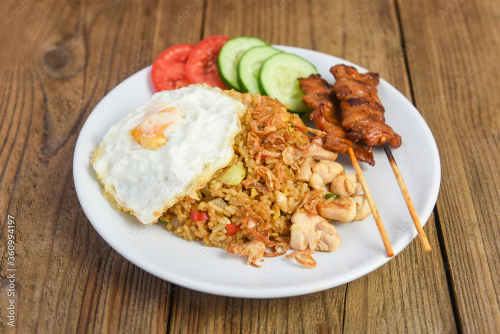 Nasi goreng fried rice chicken with egg tomato cucumber on white plate and satay with sauce - Nasi Goreng Ayam indonesian food Asian Nasi goreng fried rice chicken with egg tomato cucumber on white plate and satay with sauce - Nasi Goreng Ayam indonesian food Asian