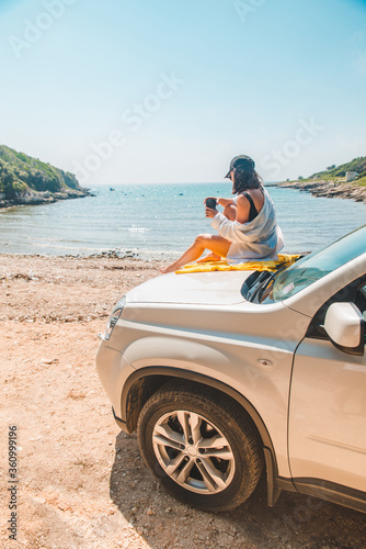 woman sitting at car hood drinking coffee enjoying view of the sea © phpetrunina14