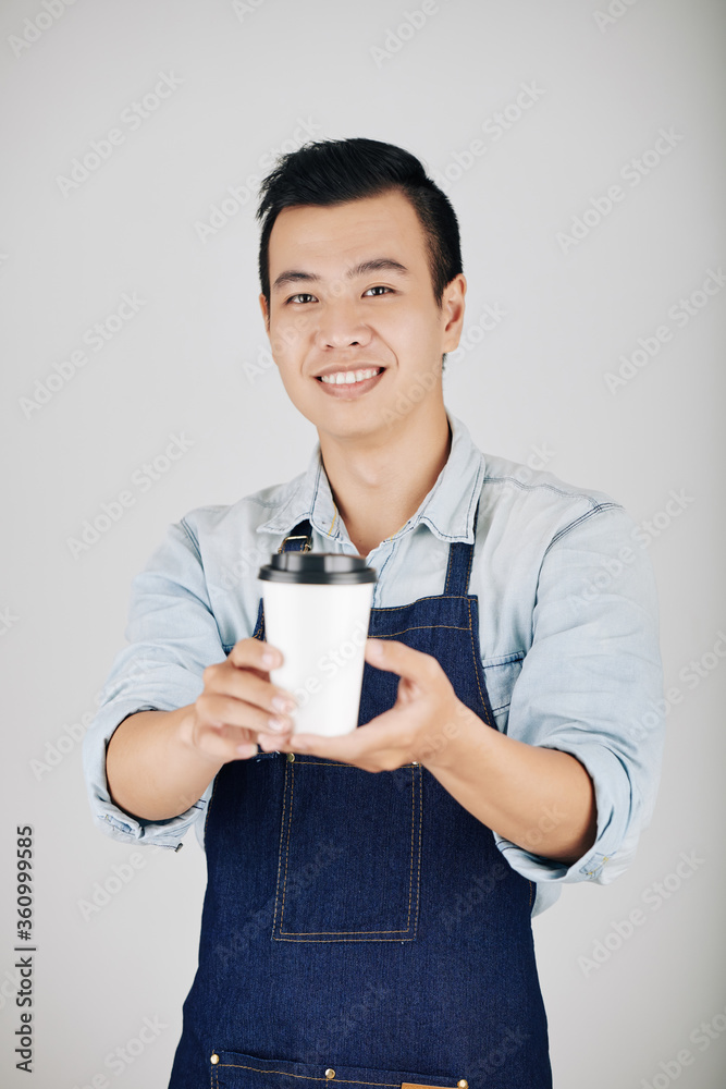 Smiling coffeeshop owner in denim apron giving cup of take out coffee Smiling coffeeshop owner in denim apron giving cup of take out coffee
