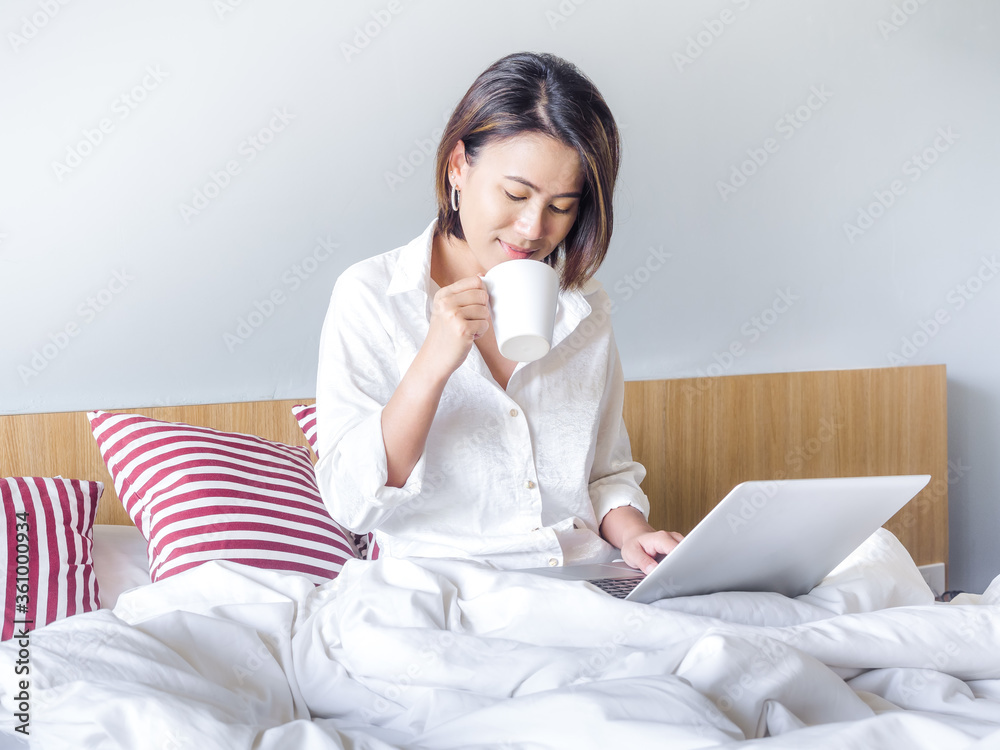 Beautiful Asian women with short hair wearing white shirt working with laptop computer on the bed in the house. Beautiful Asian women with short hair wearing white shirt working with laptop computer on the bed in the house.
