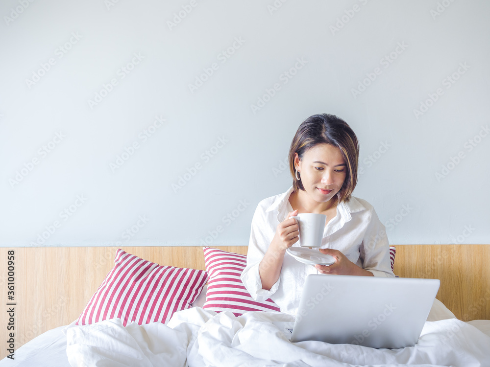 Beautiful Asian women with short hair wearing white shirt working with laptop computer on the bed in the house. Beautiful Asian women with short hair wearing white shirt working with laptop computer on the bed in the house.