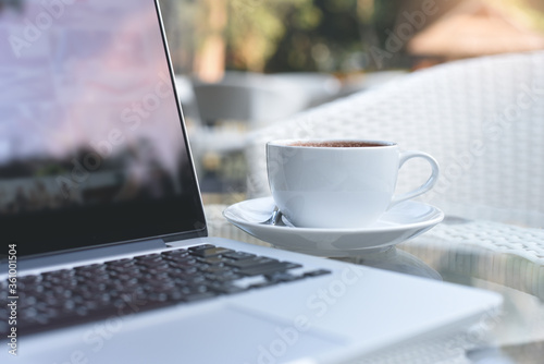 Laptop computer and cup of coffee on table with nobody for inline working from home concept