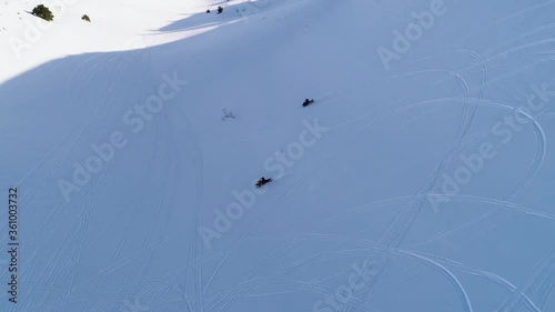 Two fast snowmobiles driving downhill on white snowy mountain in shadow on sunny day, Akoura, Lebanon, high aerial track photo