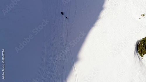 Snowmobile driving and pulling skier on white snowy mountain on sunny day, Akoura, Lebanon, high circle aerial photo