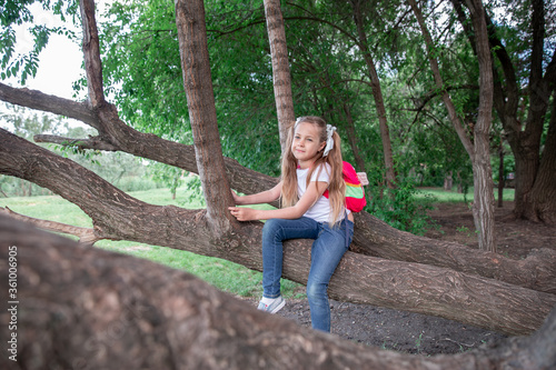 little girl with tails in green forest, in the park. The child smiles and holds a leaf.