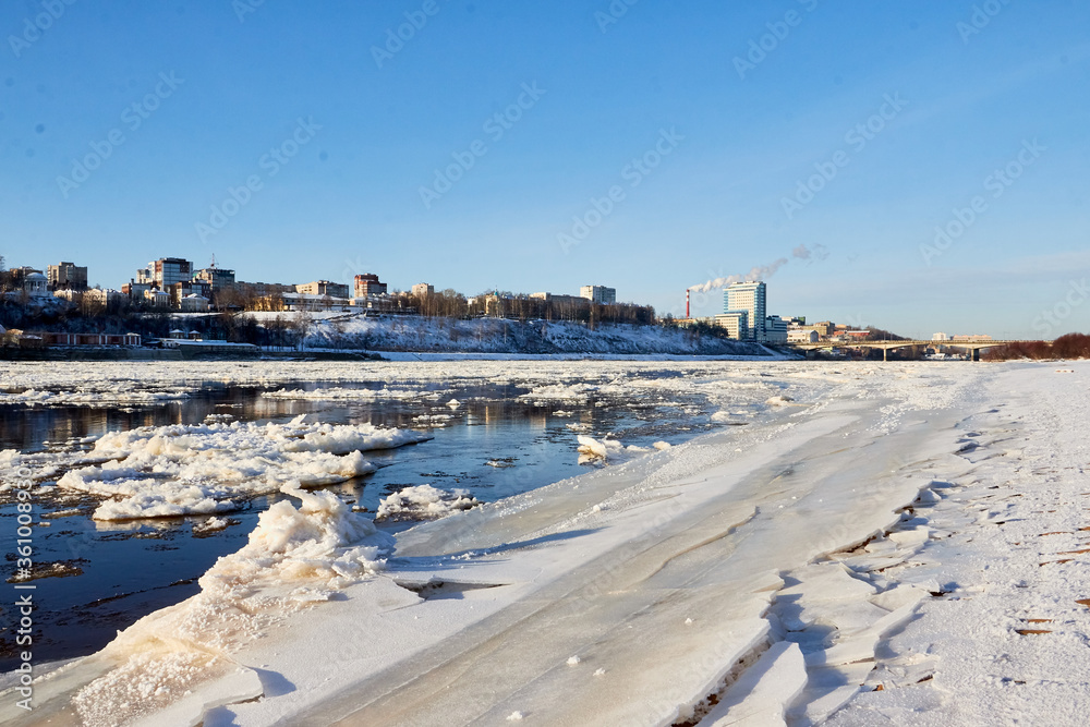 Ice drift on a river with blue high water and big water, white snow broken ice full of hummocks in it and city with houses at a background in sunny spring day. Ice drift on a river with blue high water and big water, white snow broken ice full of hummocks in it and city with houses at a background in sunny spring day.