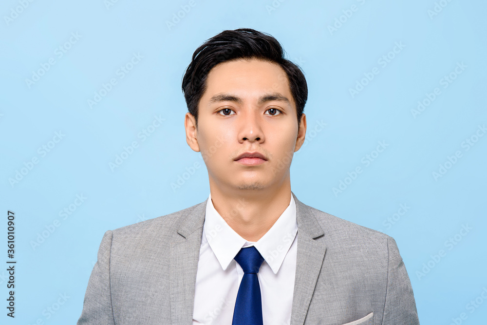 Close up portrait of serious young Asian businessman looking at camera in isolated studio blue background Close up portrait of serious young Asian businessman looking at camera in isolated studio blue background