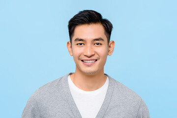 Close up portrait of happy handsome Asian man cheerfuly smiling while looking at camera in isolated studio blue background
