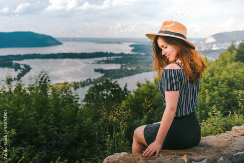 Woman traveler with long hair holding hat and looking at amazing mountains and river, wanderlust travel concept, space for text, atmospheric epic moment photo