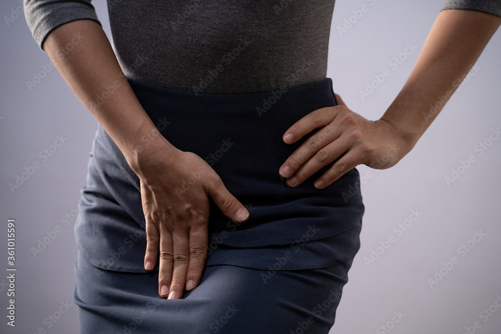 Closeup shot of woman having painful holding hands pressing her crotch  isolated on background Stock Photo