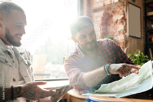 Photos Positive young men sitting at table in sunlight and discussing forthcoming trip