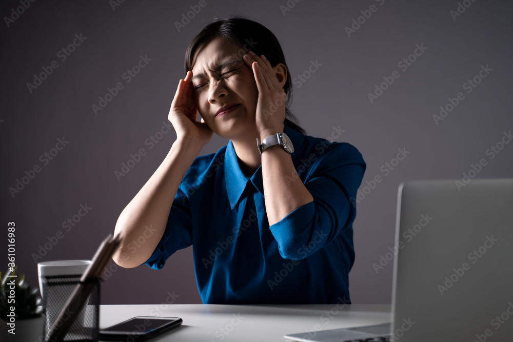 Asian woman in blue shirt was sick with headache working on a laptop at office.