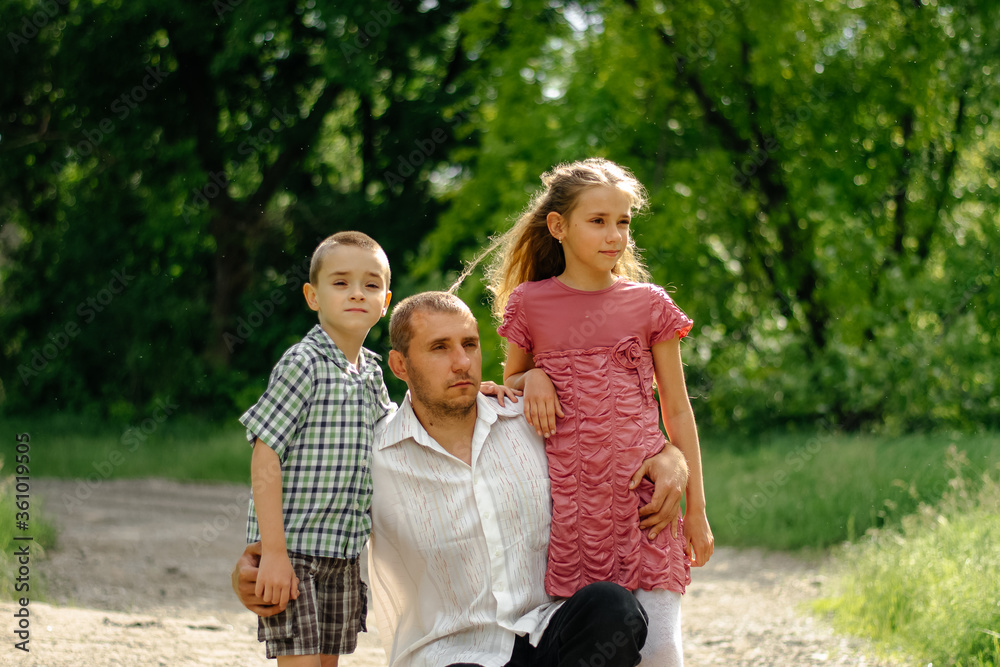 Obraz premium Amazing day. Happy family. Father and children look into the distance, against the background of green trees. Blurred backgroun