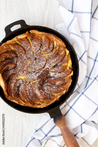 Homemade Apple Dutch Pannekoek Pancake in a cast-iron pan on a white wooden surface, top view. Overhead, from above, flat lay. photo