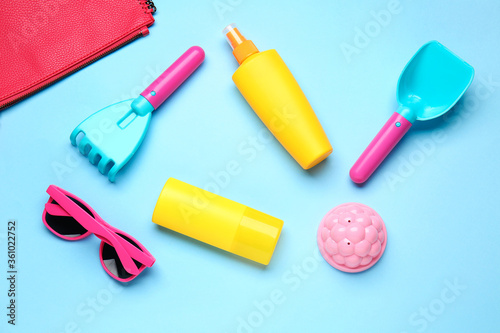 Sunscreen cream with beach sand toys and sunglasses on color background