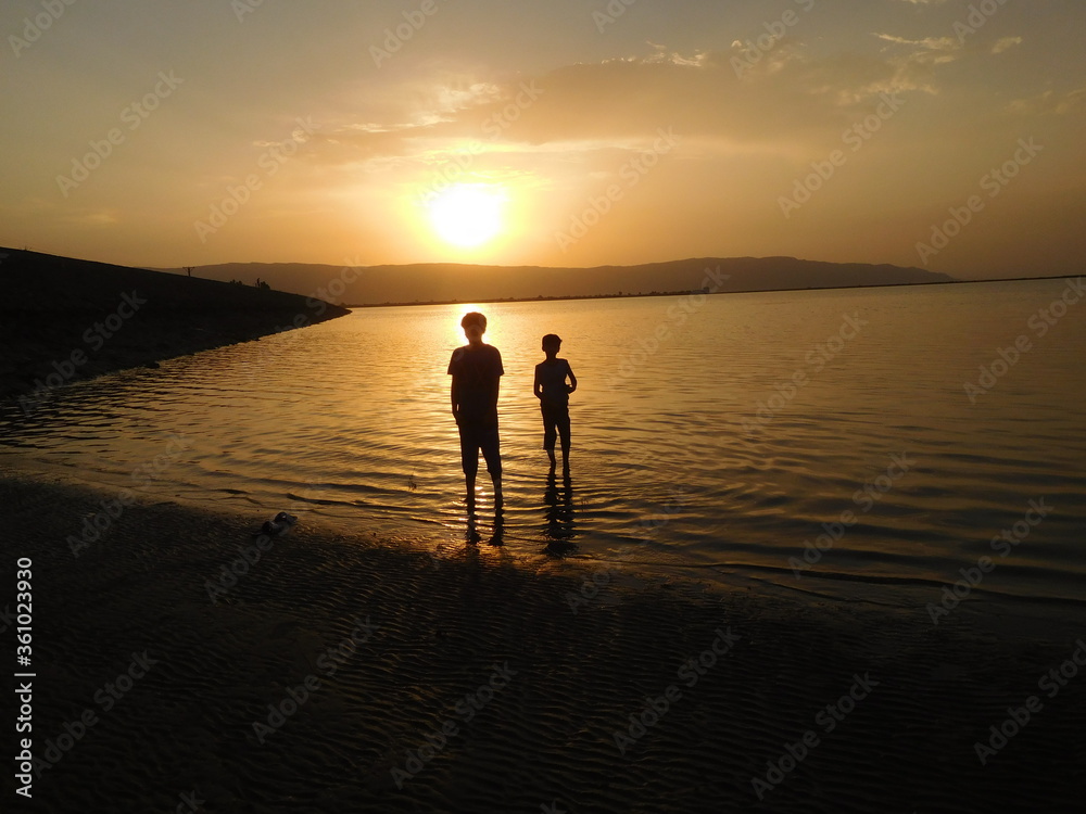 two boys looking at sun. silhouette of kids on beach at sunrise.