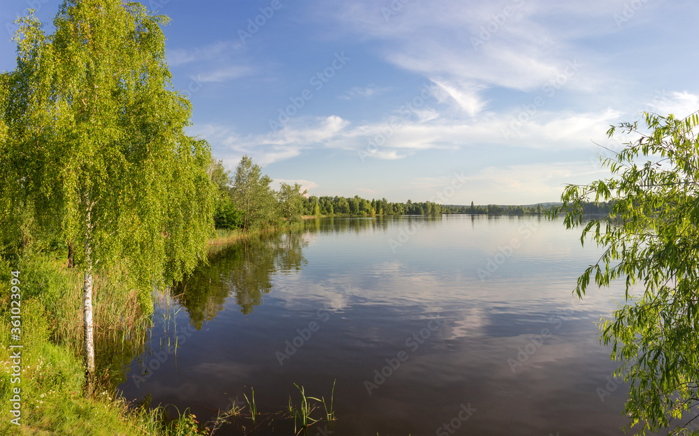 Lake with shores overgrown with trees in summer evening