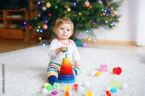 Adorable cute beautiful little baby girl playing with educational toys at home or nursery. Happy healthy child having fun with colorful wooden rainboy toy pyramid. Kid learning different skills. photo