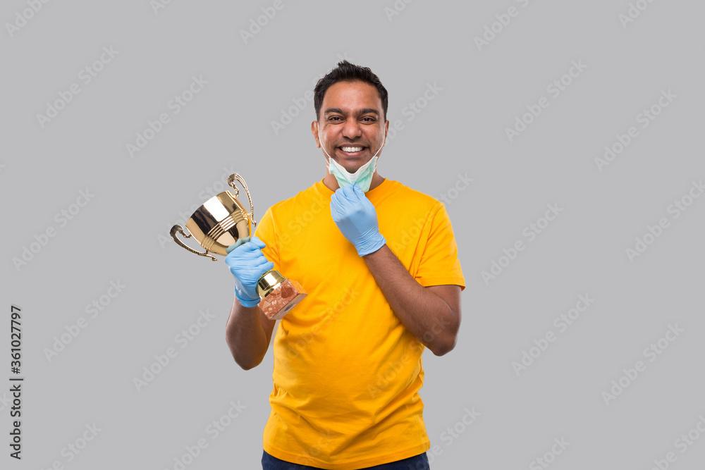 Indian Man Holding Trophy in Hands Wearing Medical Mask and Gloves Isolated. Man Taking off Medical Mask Indian Man Holding Trophy in Hands Wearing Medical Mask and Gloves Isolated. Man Taking off Medical Mask