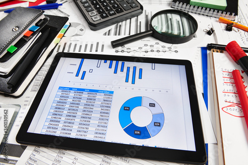 Top view of office employee's desk - work with tablet pc computer and financial reports, analysis and accounting, tables and graphs, various office items for bookkeeping