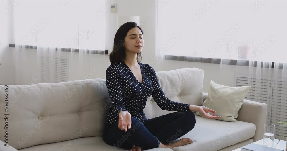 Asian ethnicity millennial woman sit cross-legged on couch with folded fingers, closed eyes do inhale exhale exercise breathing fresh air enjoy mindfulness inner harmony, meditation yoga time concept Asian ethnicity millennial woman sit cross-legged on couch with folded fingers, closed eyes do inhale exhale exercise breathing fresh air enjoy mindfulness inner harmony, meditation yoga time concept