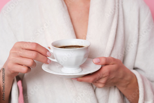 Coffe mood. Woman in white bath robe is holding a cup of coffee. Studio shoot on pink background.