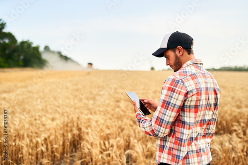 Smart farming using modern technologies in agriculture. Man agronomist farmer holding digital tablet computer standing in a wheat field and using apps, internet for business management and analytics.