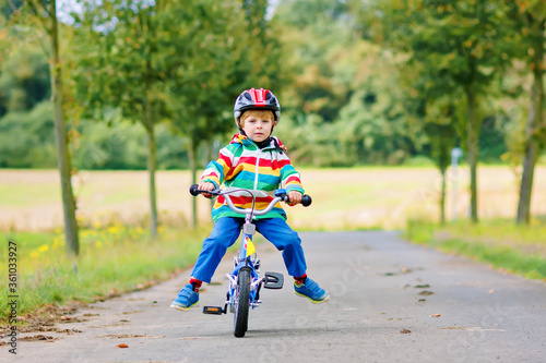 Fototapeta Naklejka Na Ścianę i Meble -  Little cute kid boy on bicycle on summer or autmn day. Healthy happy child having fun with cycling on bike. Active leisure for children. Safe helmet on boy's head. In colorful clothes
