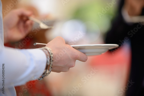 Mani di un invitato che sorreggono piatto e forchetta in una cena in piedi all’aperto 