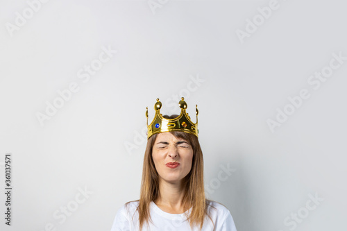 Young woman with a crown on her head and closed eyes on a light background. Emotion laughter, surprise, shock. Concept of a queen, luck, wealth, gain, victory, dream, goal, aspiration. Banner