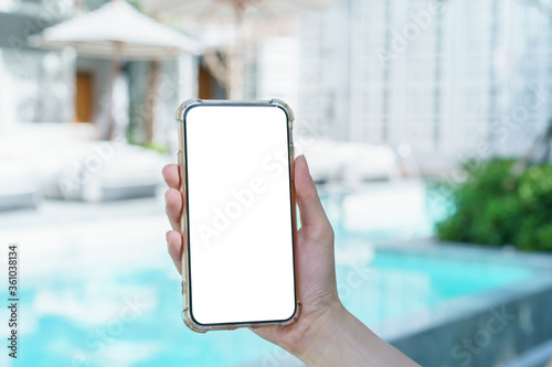 Fotografia Woman hand holding blank white screen mobile phone near swimming  pool