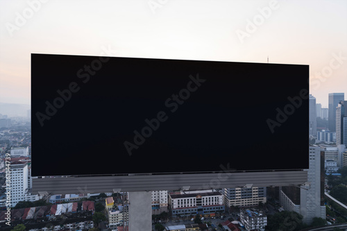 Blank black road billboard with Kuala Lumpur cityscape background at sunset. Street advertising poster, mock up, 3D rendering. Front view. The concept of marketing communication.