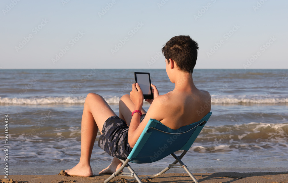 boy reads an e-book on the seashore in summer