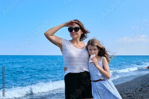 Happy mom and daughter kid hugging together on beach, copy space