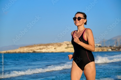 Happy mature woman running along the beach, copy space