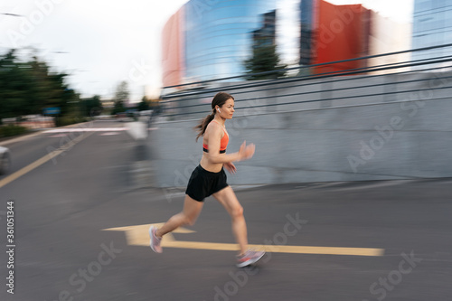 Young woman sprinting in the morning outdoors. Side view of female runner in motion working out in the city.