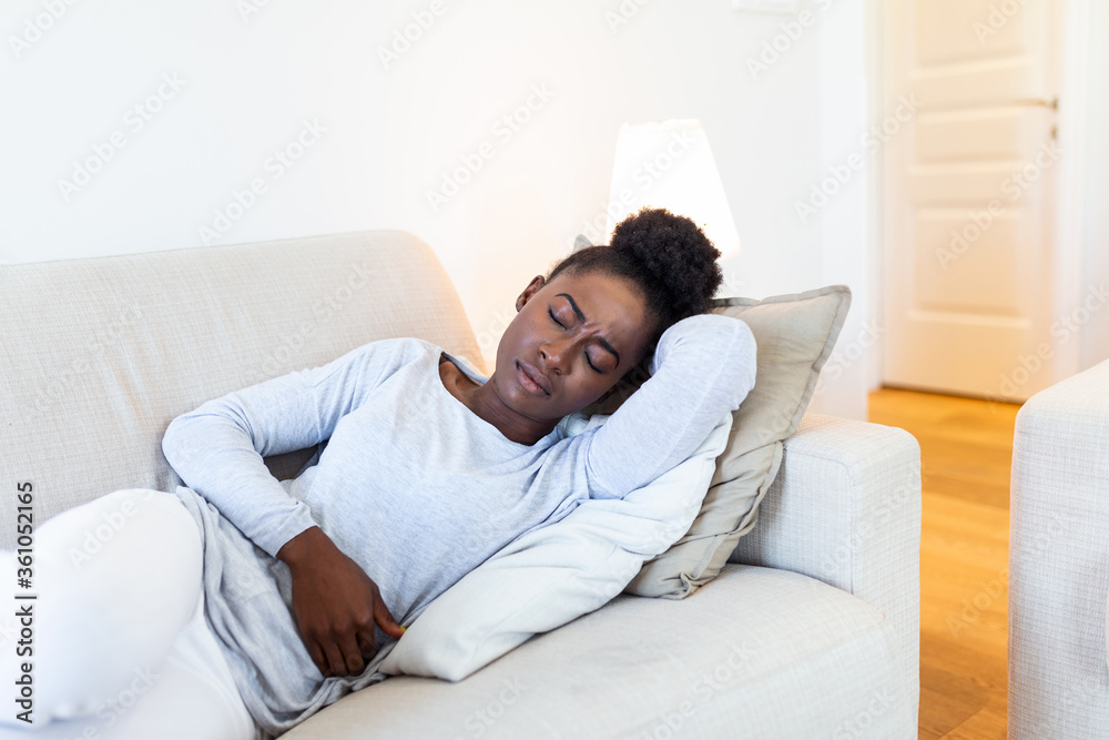 Woman lying on sofa looking sick in the living room. Beautiful young woman lying on bed and holding hands on her stomach. Woman having painful stomachache on bed, Menstrual period
